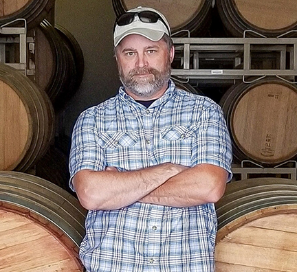 Derek_Irwin_barrel_room_cropped man in front of stacked wine barrels
